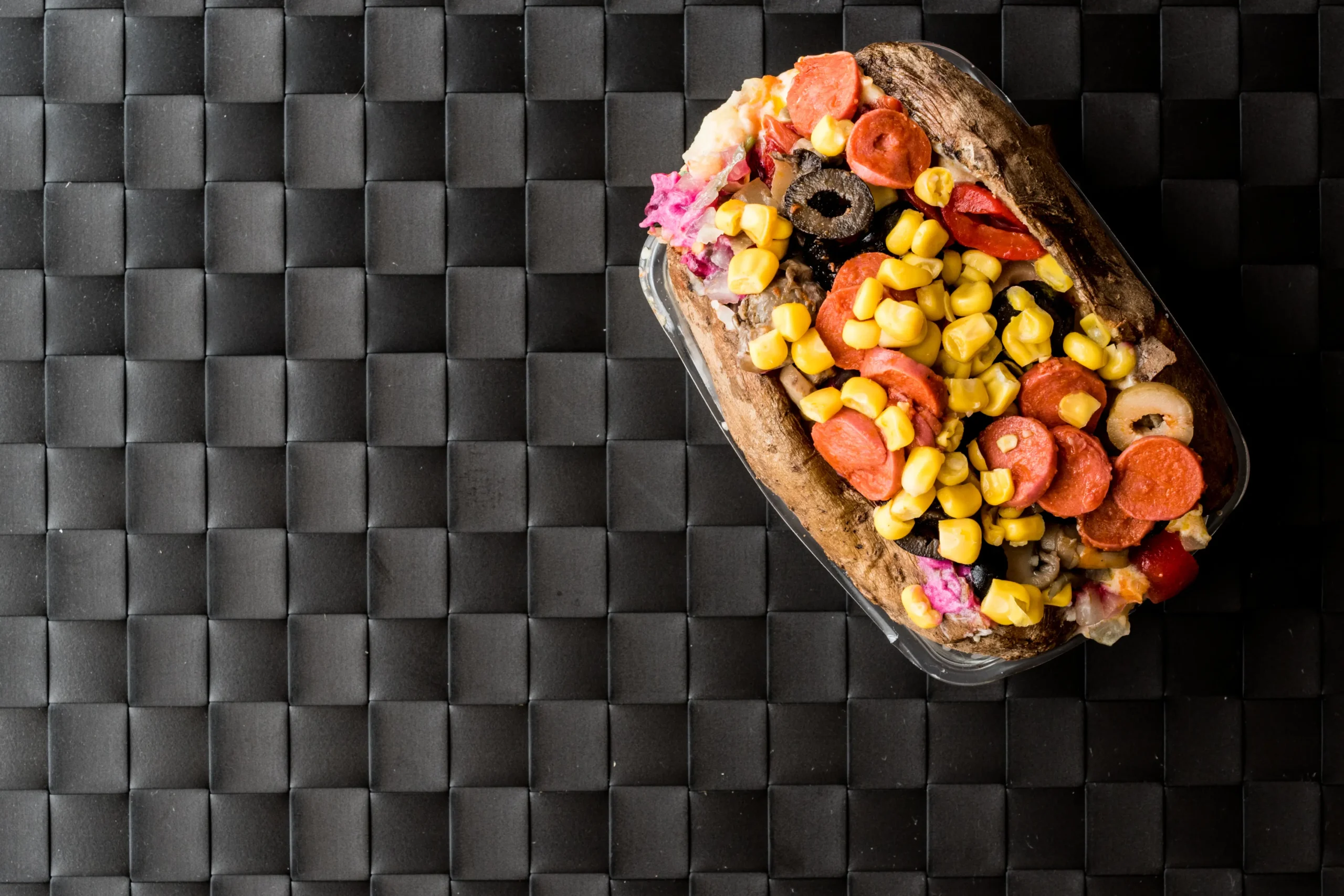 Kumpir Turkish loaded baked potato with corn sausage cheese and toppings on black background